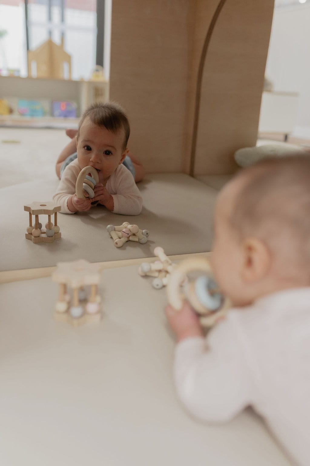Two babies lying on their tummies playing with wooden toys