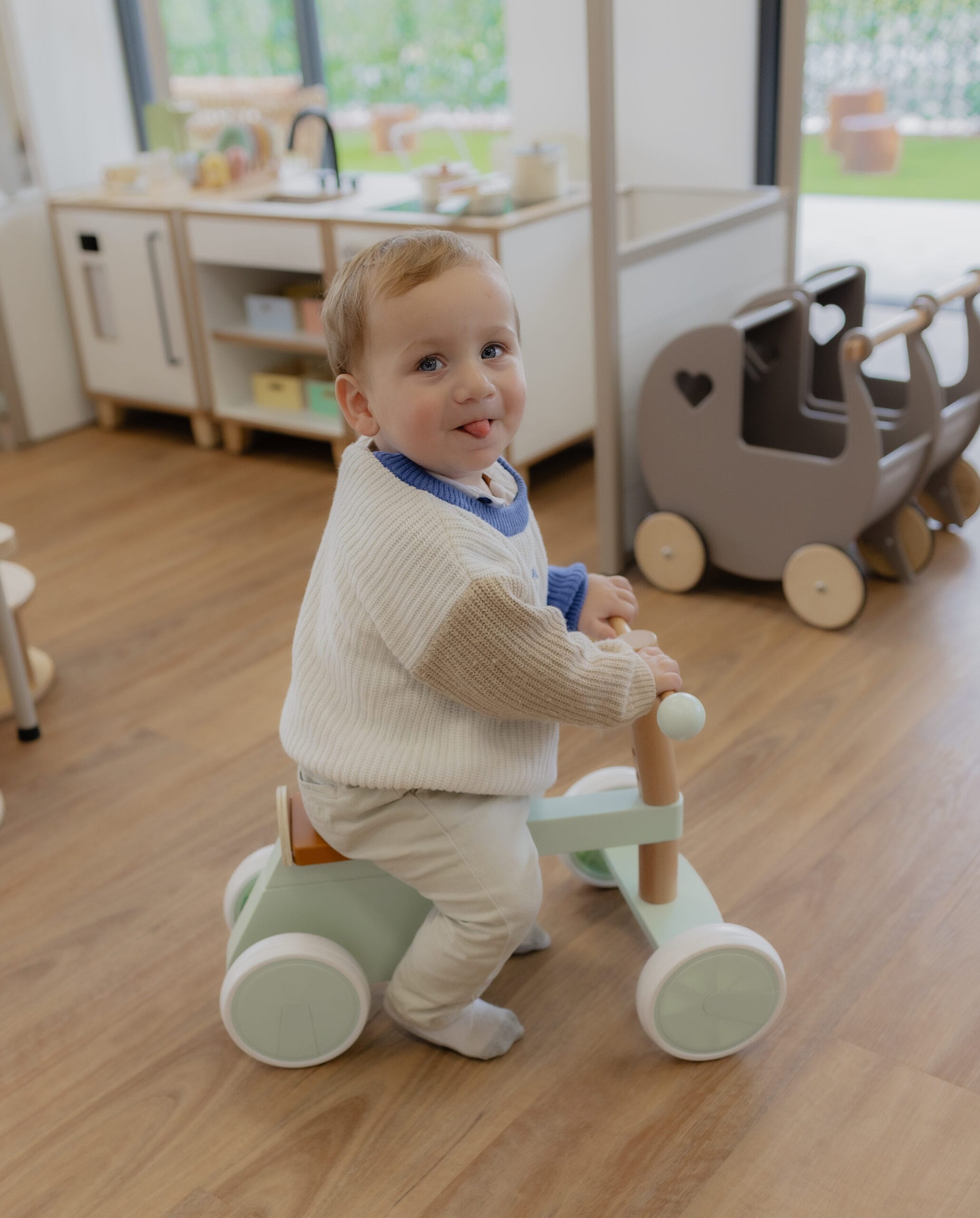 A toddler sticking out his tongue while riding a wooden balance bike