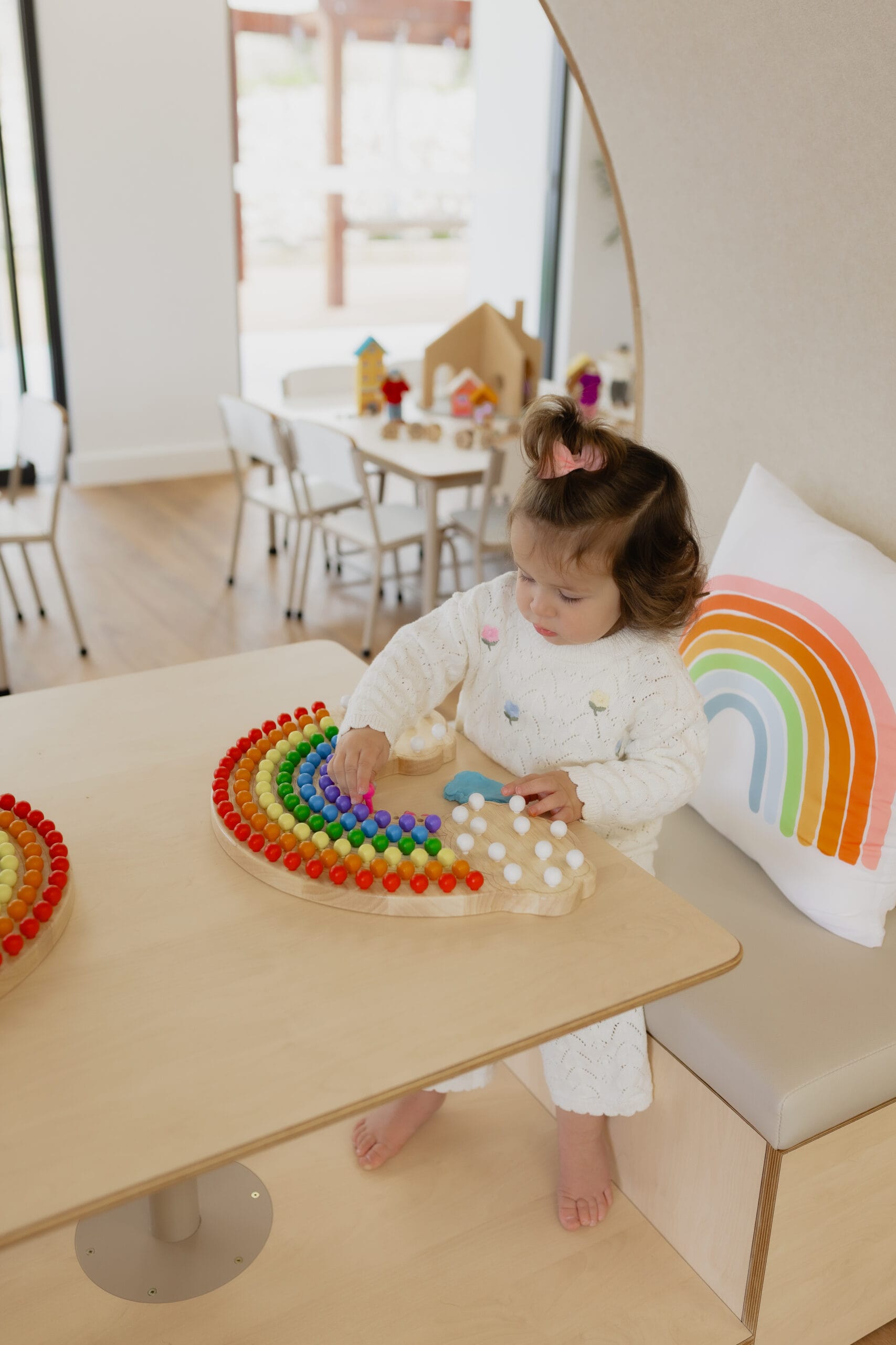 A toddler seated at a table playing with a wooden rainbow shape sorter puzzle in the Sun Room