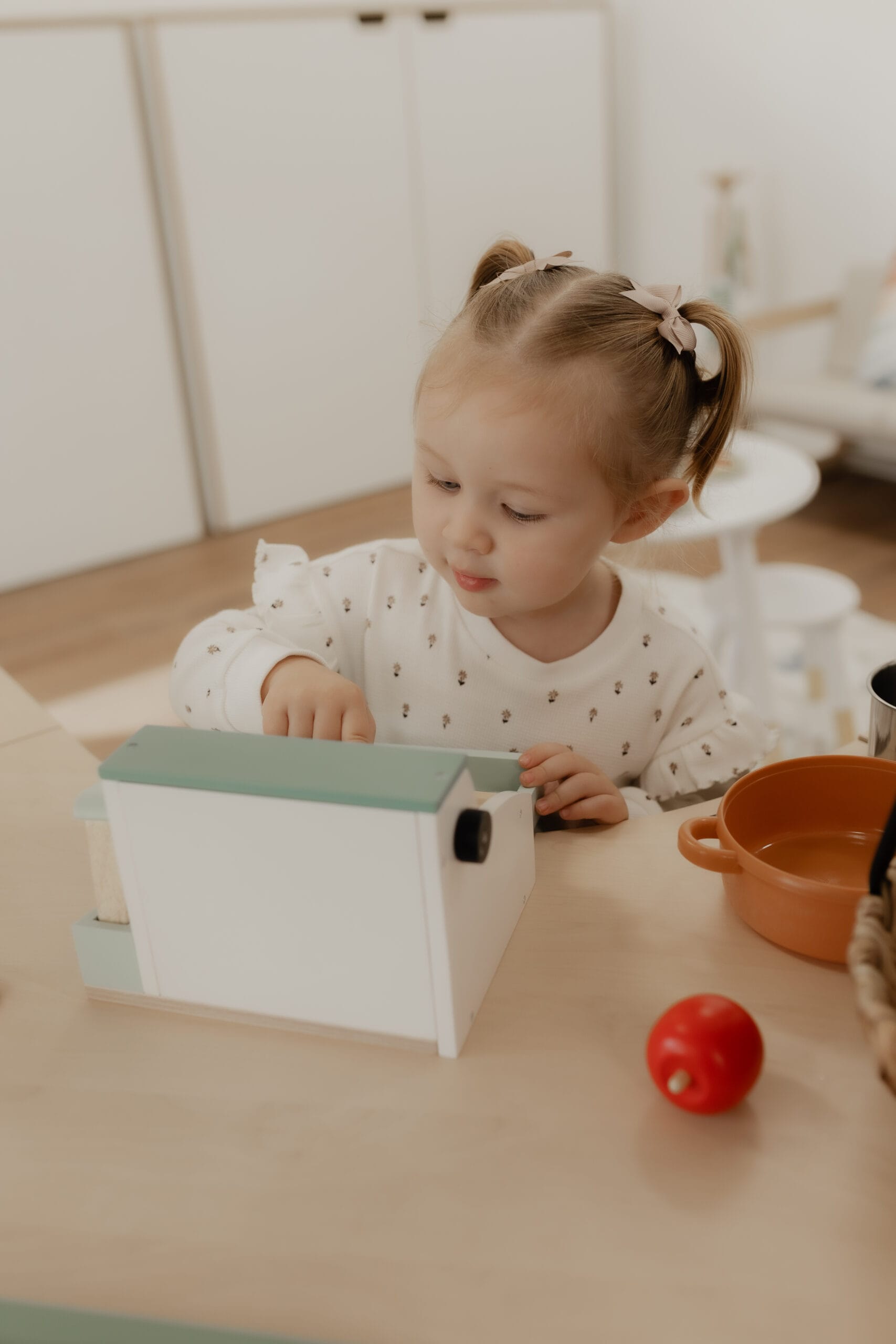 A girl playing with a wooden toy house and pretend play food at a table