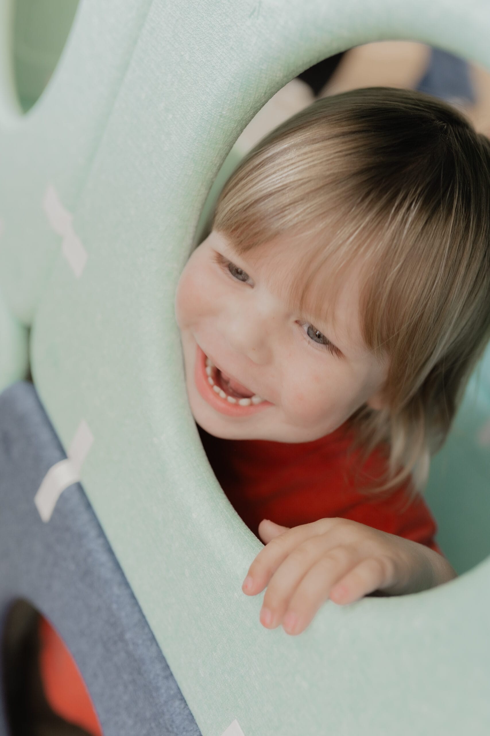 A child laughing while peeking through a soft play climbing structure