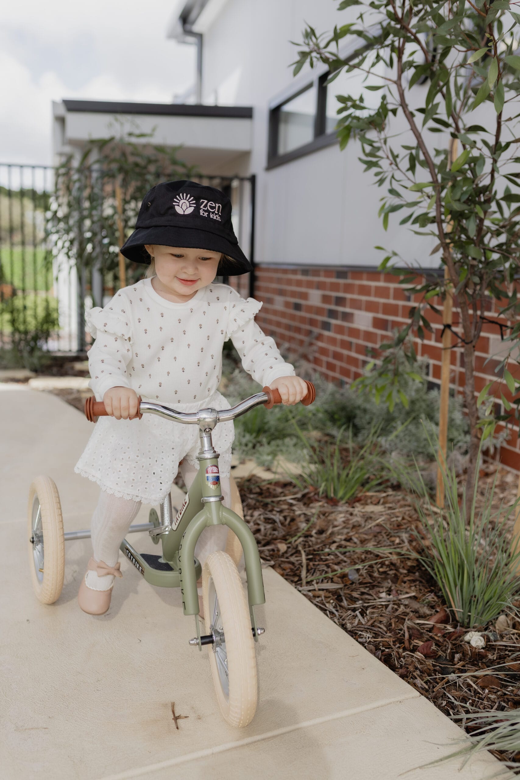 A girl wearing a black bucket hat riding a balance bike outdoors