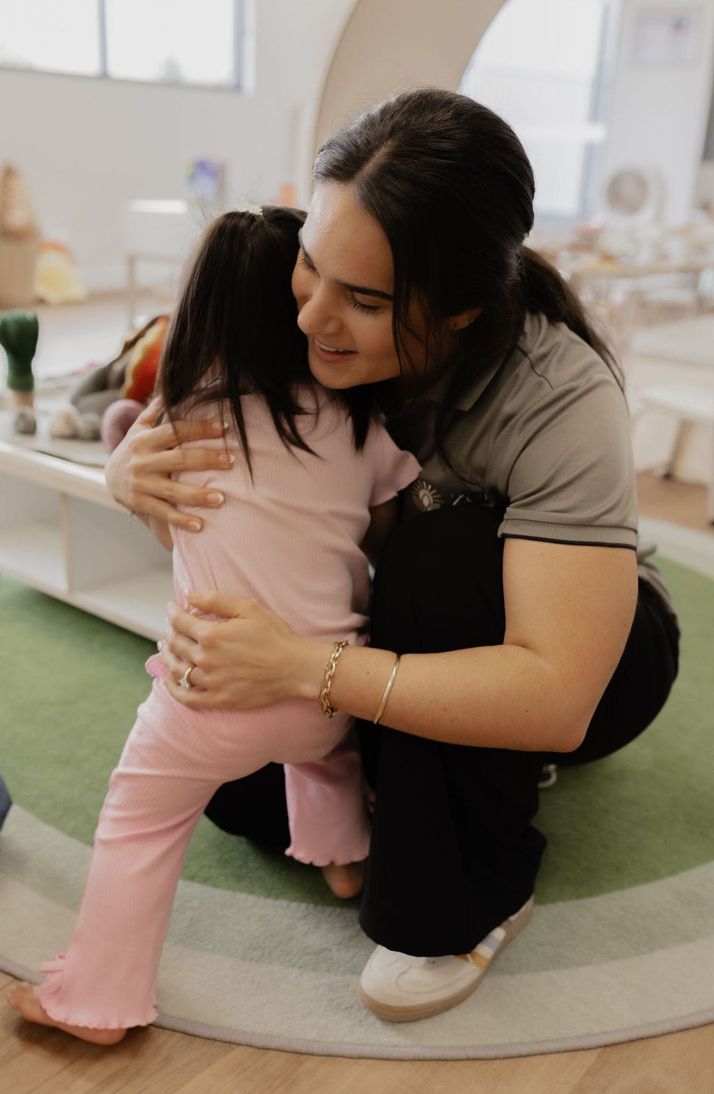An educator giving a warm hug to a child in the playroom