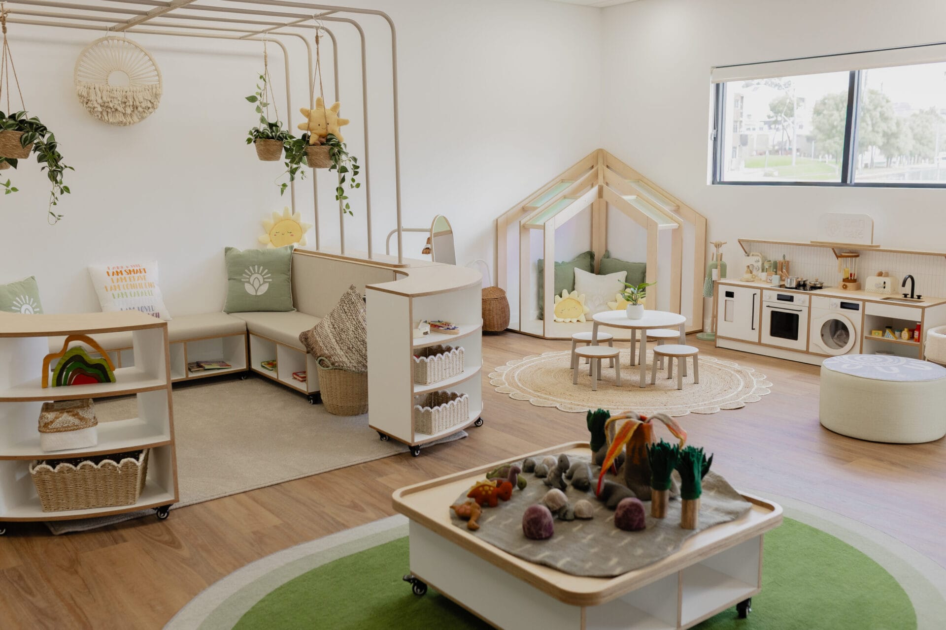 An empty learning room with a play kitchen, sensory table, and cozy play house