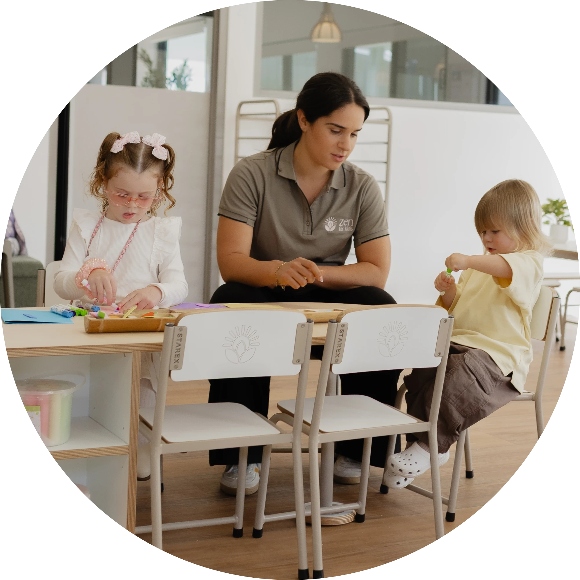 An educator sitting with two children doing a craft activity at a table