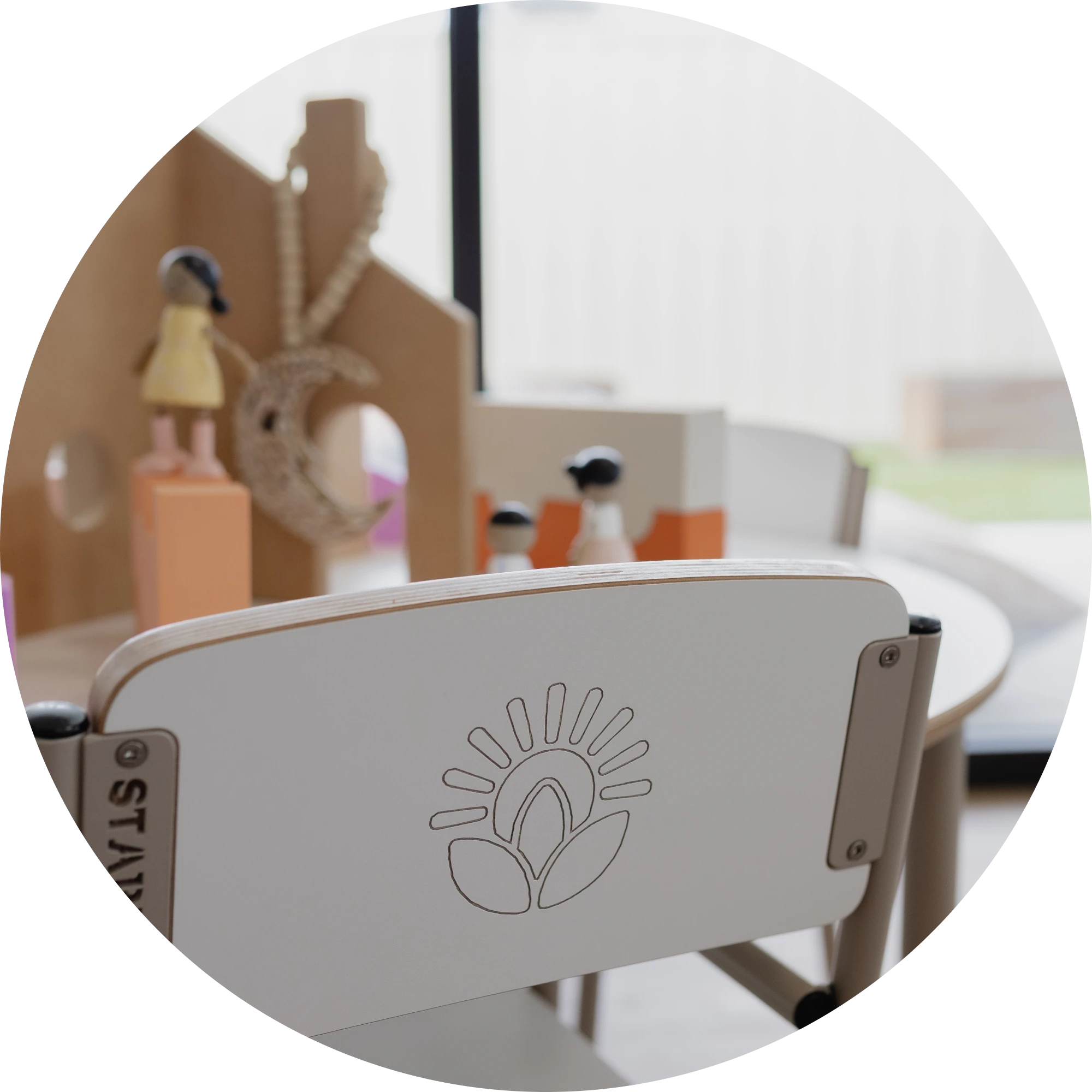 A chair with the Zen for Kids logo engraved, with wooden peg dolls in the background