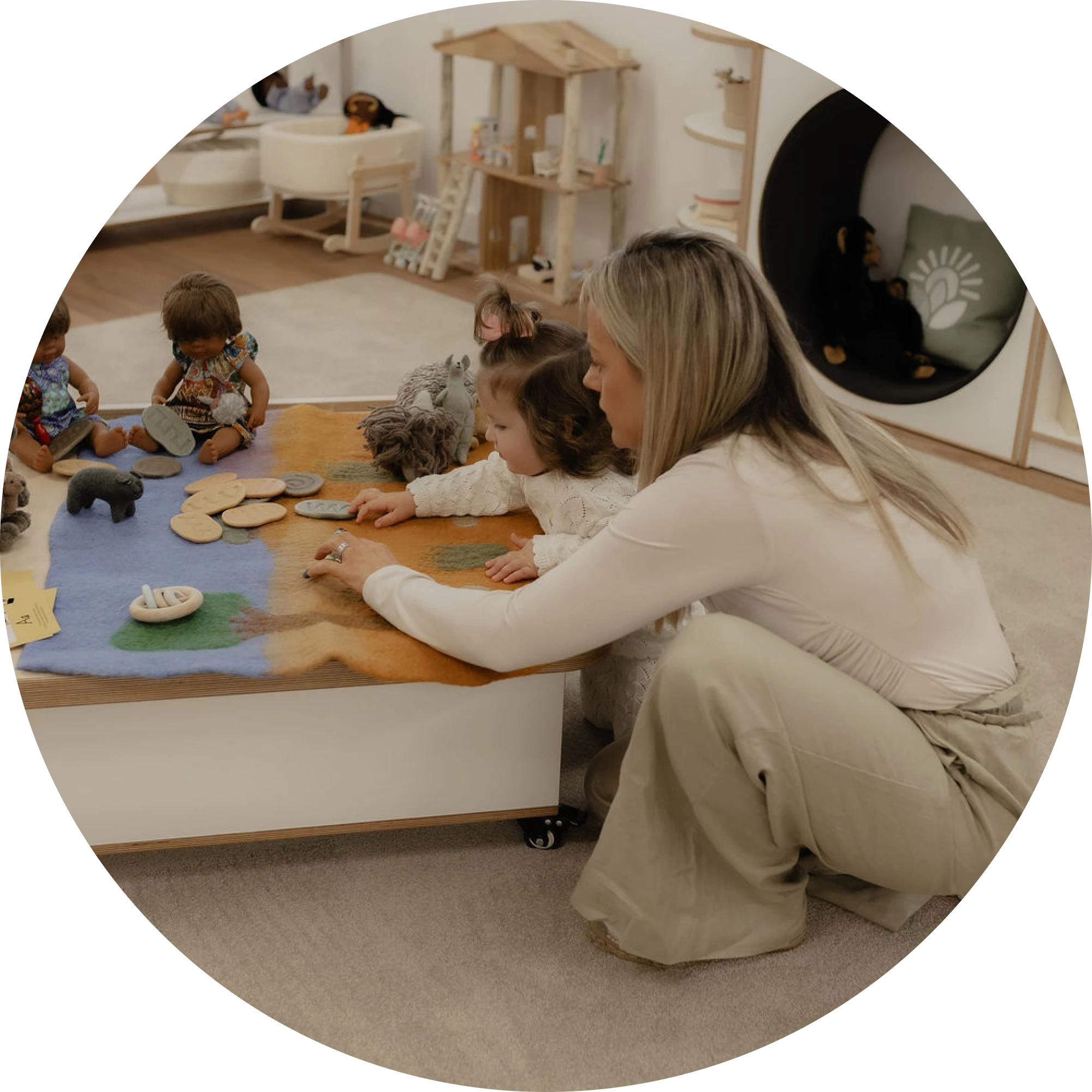 An educator kneeling beside children exploring felt play mats with animal figures